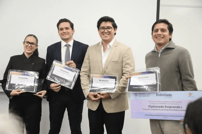 Cuatro personas posan con diplomas en un evento de entrega de premios.