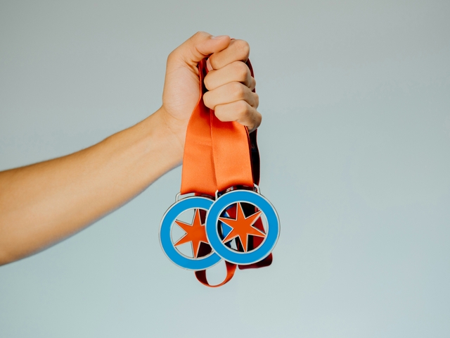 Una mano sostiene dos medallas con cintas naranjas.
