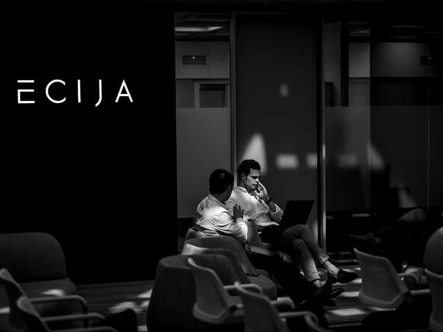 Dos personas conversan en un ambiente moderno y minimalista con el logo de ECIJA visible.
