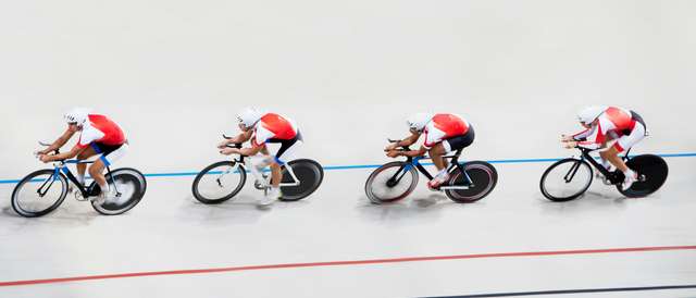 Cuatro ciclistas compiten en una pista de ciclismo de velocidad.
