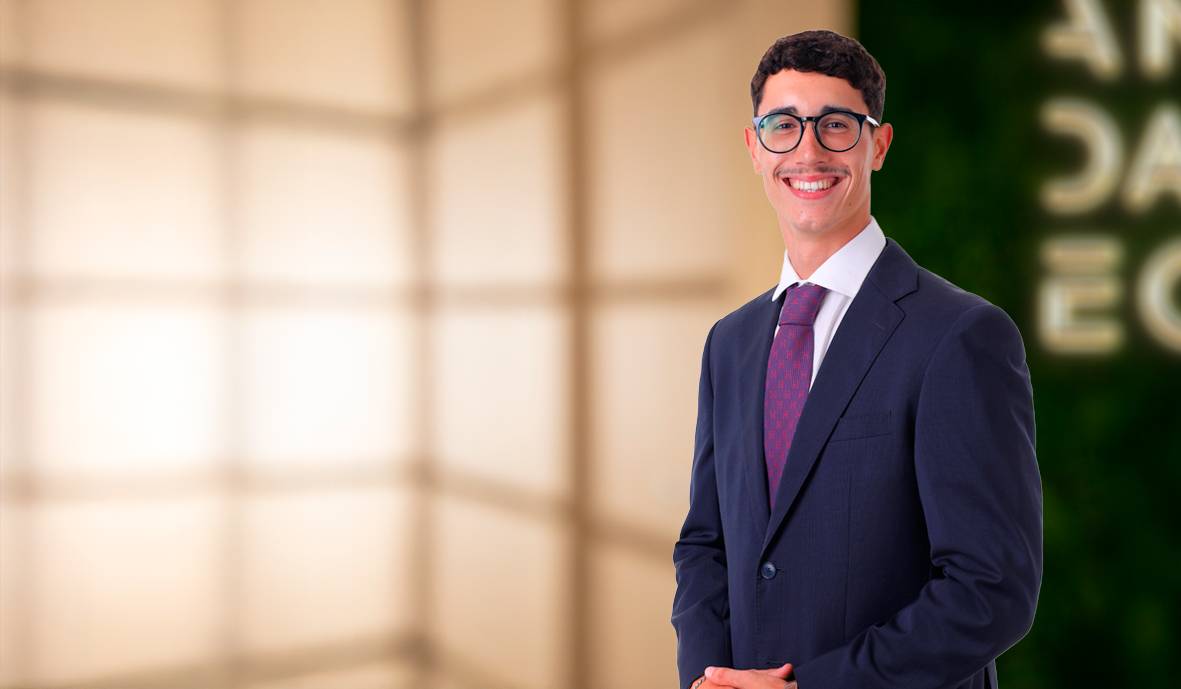Un hombre sonriente vestido con un traje formal posa frente a un fondo iluminado.