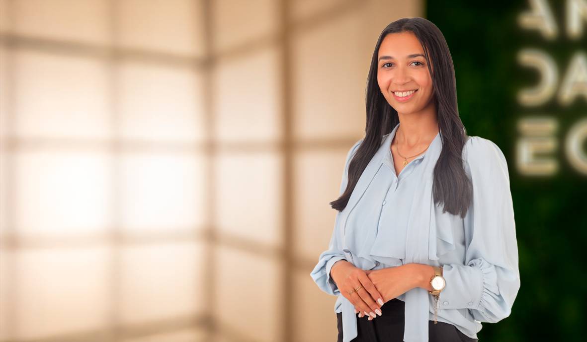 Una mujer sonriente está de pie frente a un fondo de luz suave.