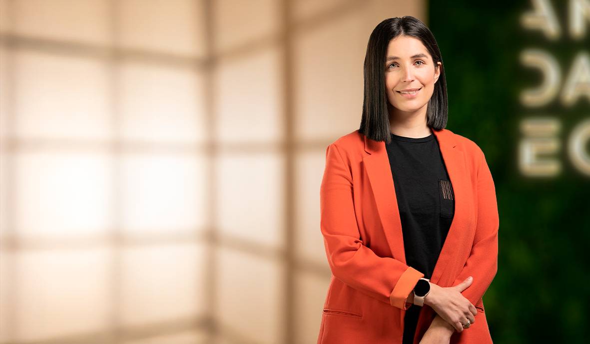 Una mujer sonriente viste un abrigo naranja frente a un fondo difuso.