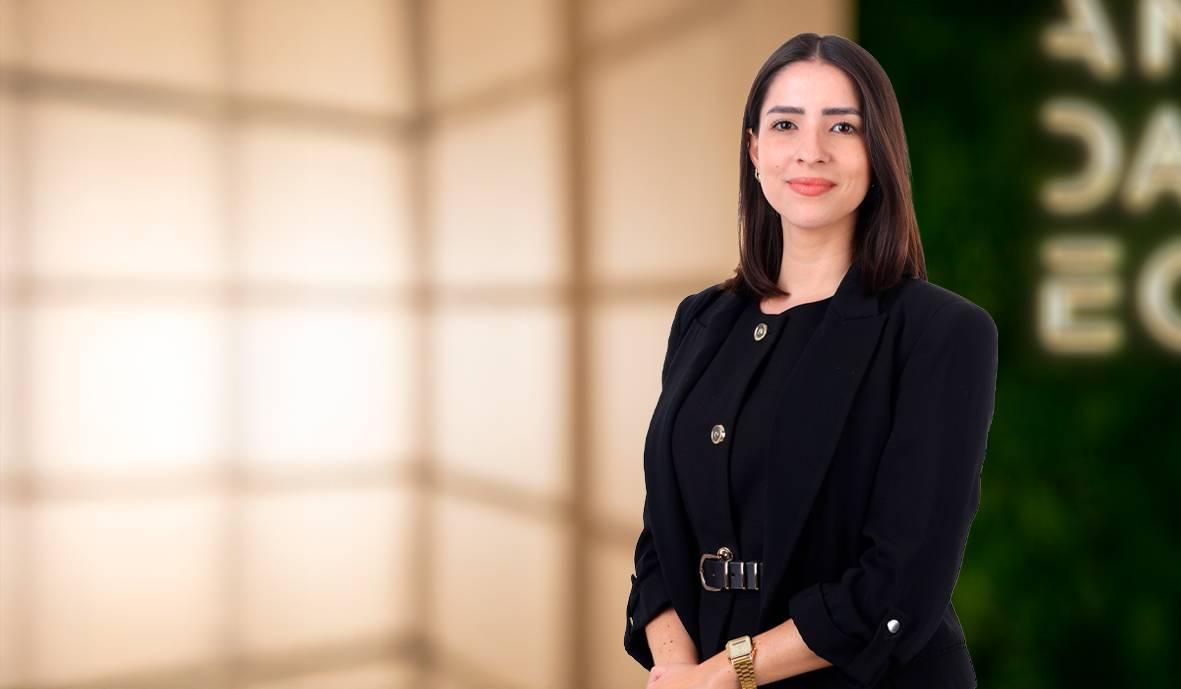 Una mujer sonriente vestida de negro posa frente a un fondo iluminado.