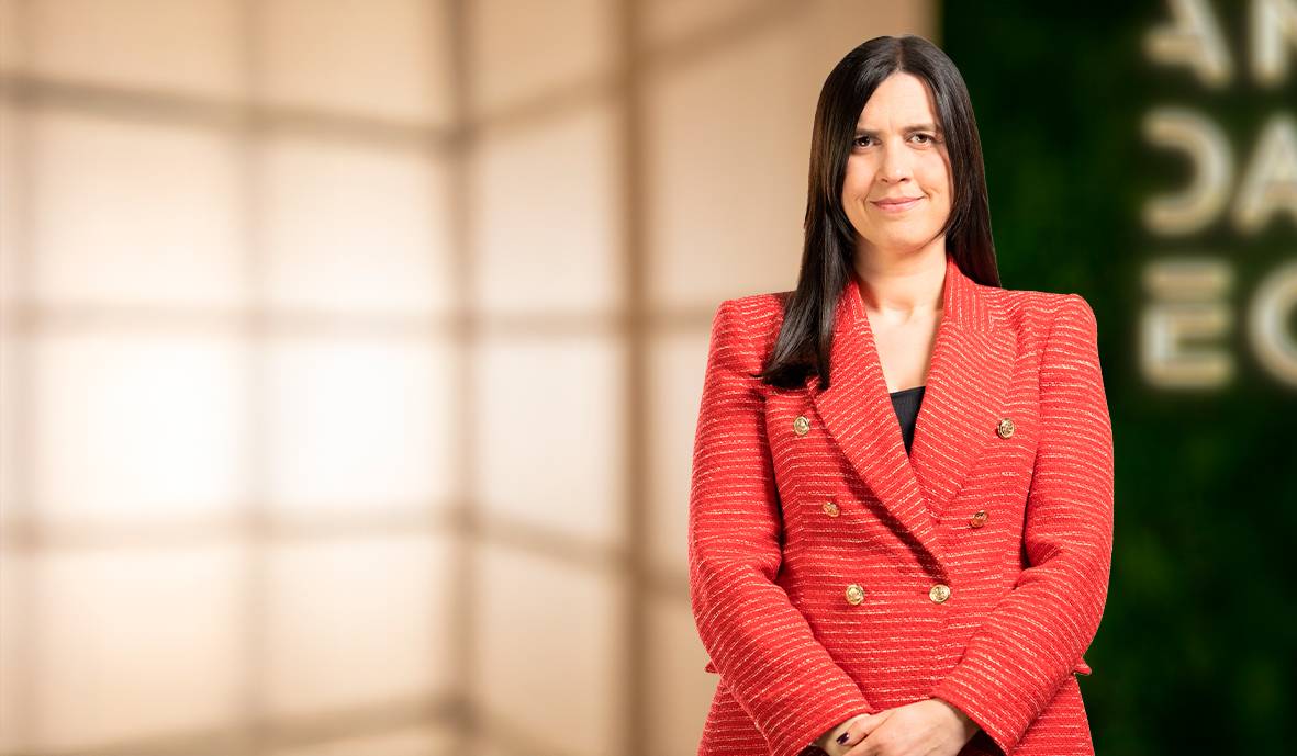 Una mujer sonriente vestida con una chaqueta roja posa frente a un fondo difuso.