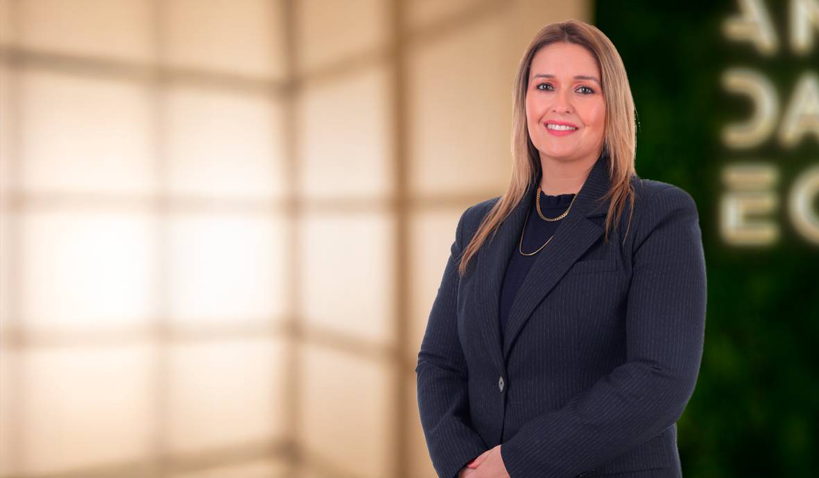 Una mujer sonriente está de pie frente a un fondo difuso y elegante de colores suaves.