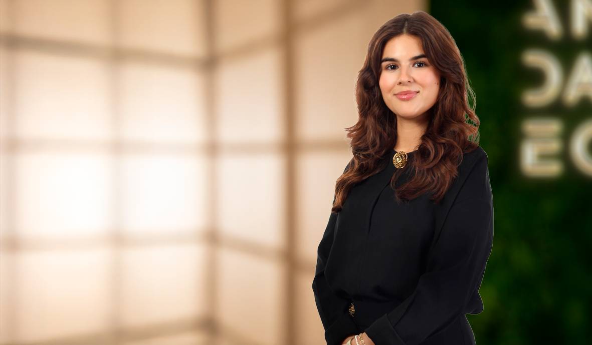 Mujer joven con cabello rizado, vestida de negro, sonriendo frente a un fondo difuso.