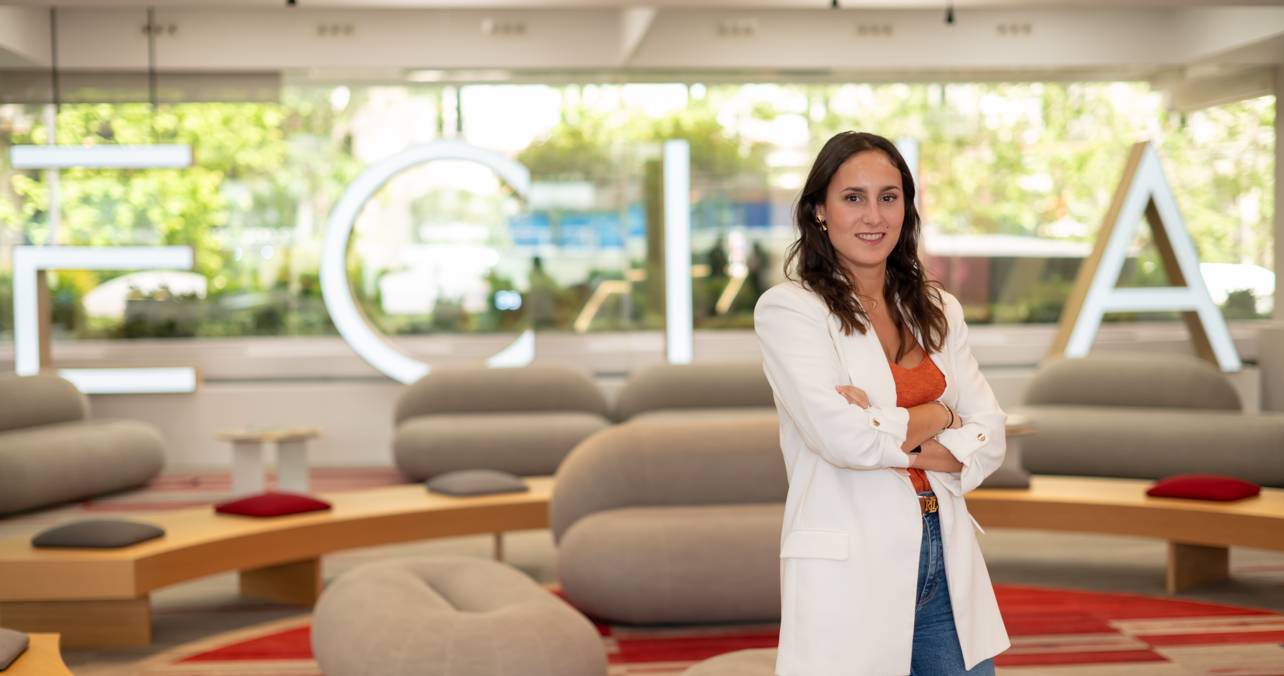 Una mujer sonriente posando en un ambiente moderno con letras grandes que dicen 'ECIJA' al fondo.