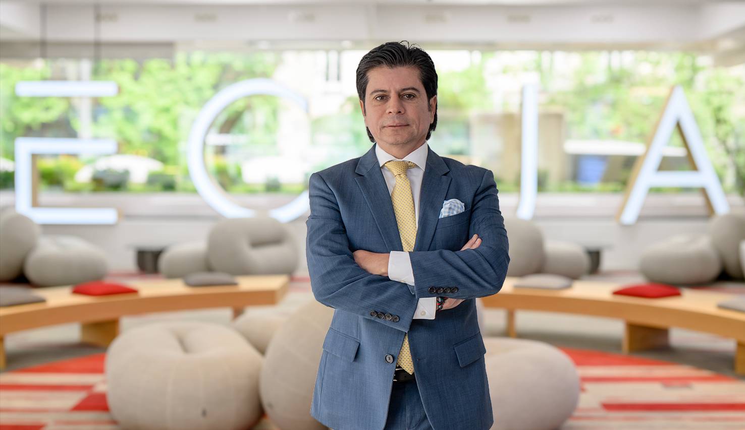 Un hombre de traje está posando con los brazos cruzados en un ambiente moderno y luminoso.