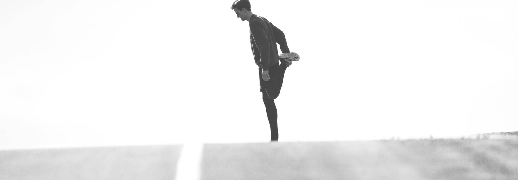 Una persona estirándose en una carretera vacía bajo un cielo claro.