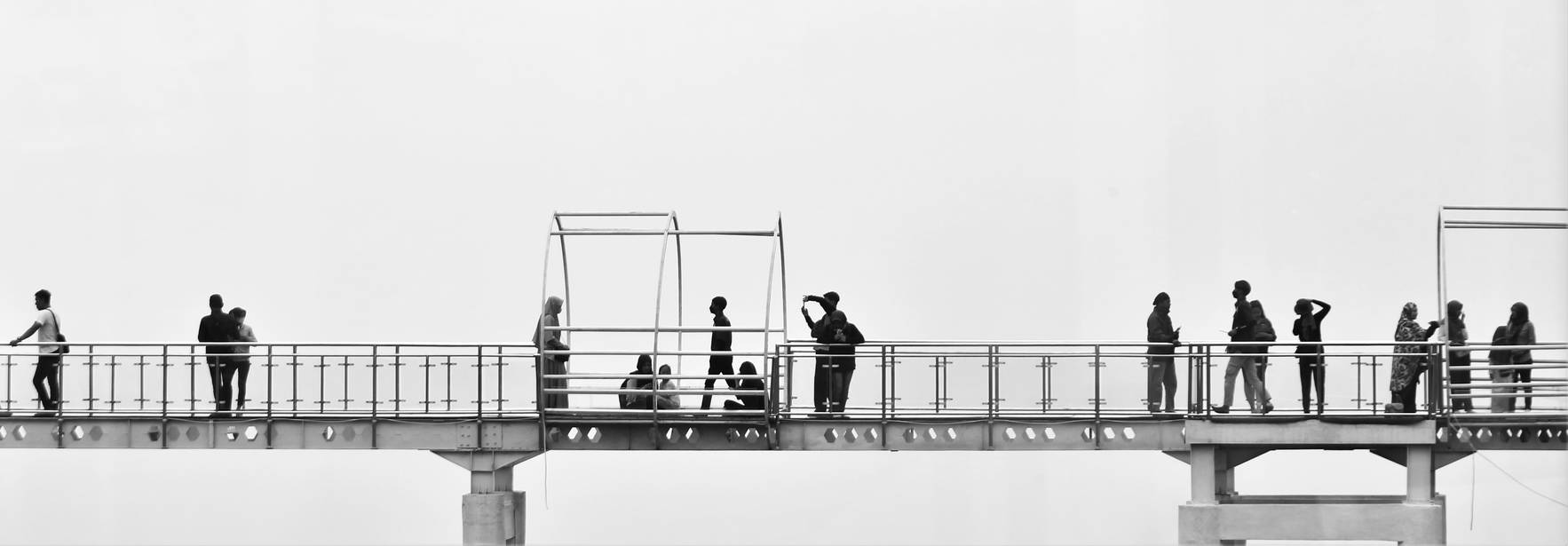 Un puente con varias personas en movimiento y estructuras para sentarse bajo una atmósfera brumosa.