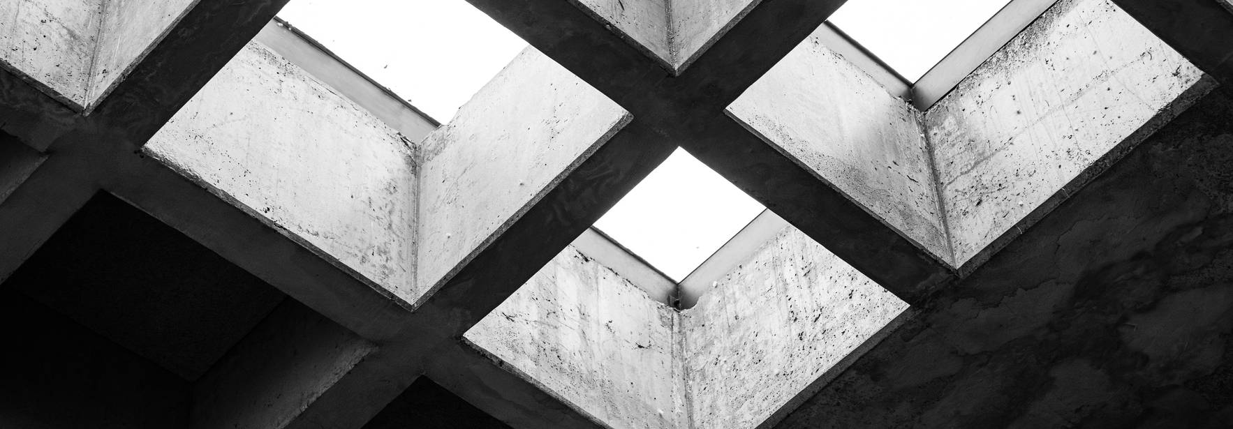Una vista desde abajo de un techo de concreto con claros rectangulares que dejan pasar la luz.