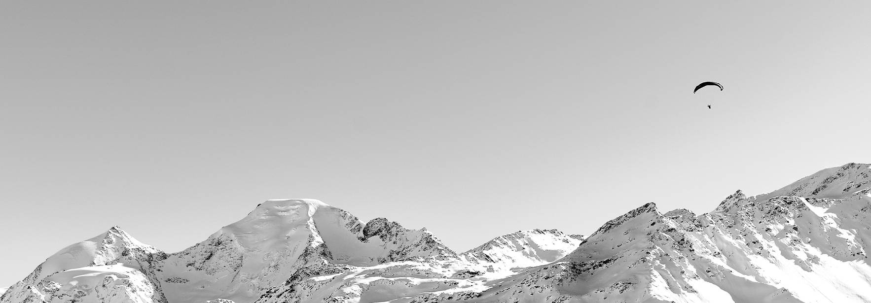 Un parapente sobrevuela montañas nevadas bajo un cielo claro.