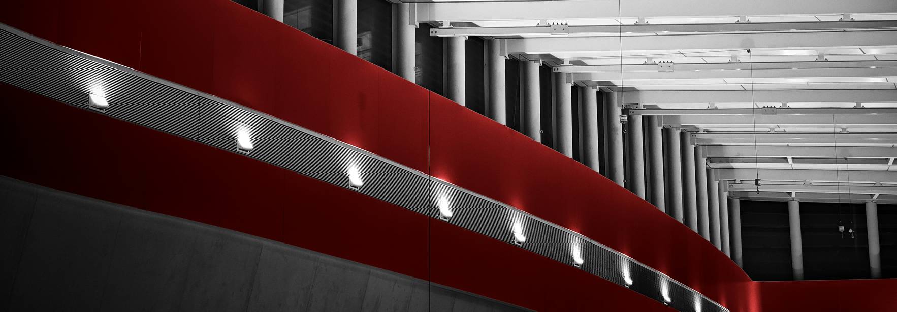 La imagen muestra un interior moderno con techos altos y elementos arquitectónicos en colores blanco y rojo.