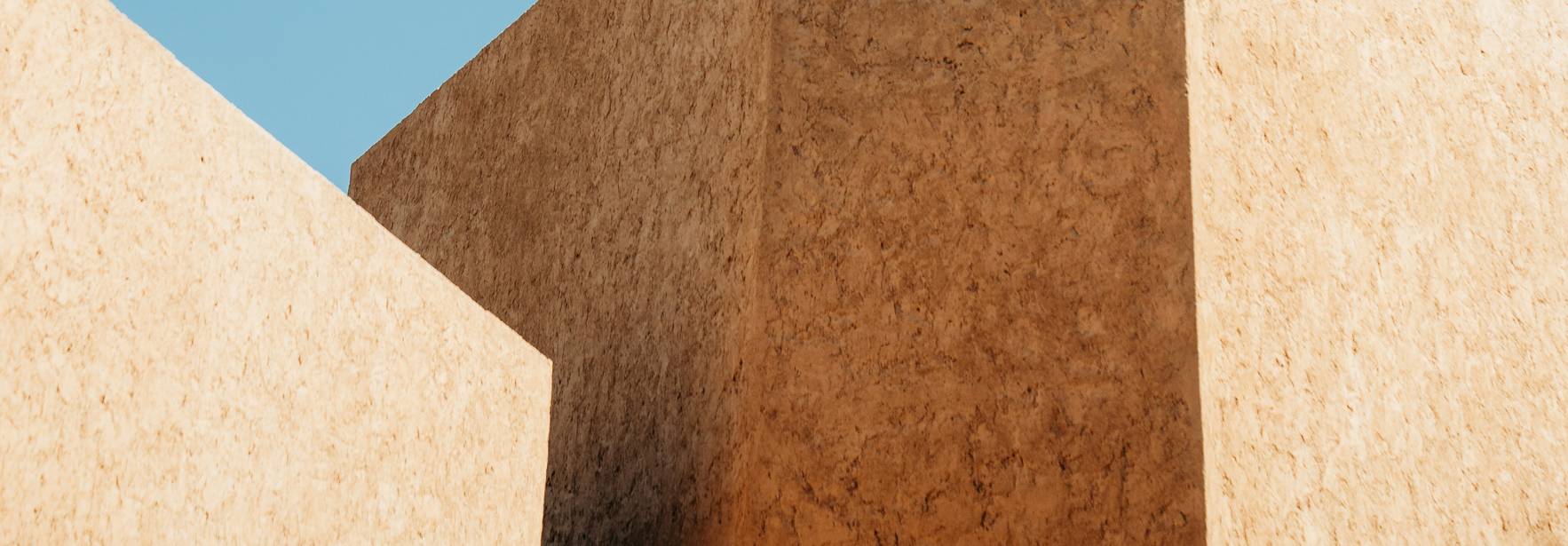 La imagen muestra unas estructuras geométricas en tonos beige contra un cielo azul claro.