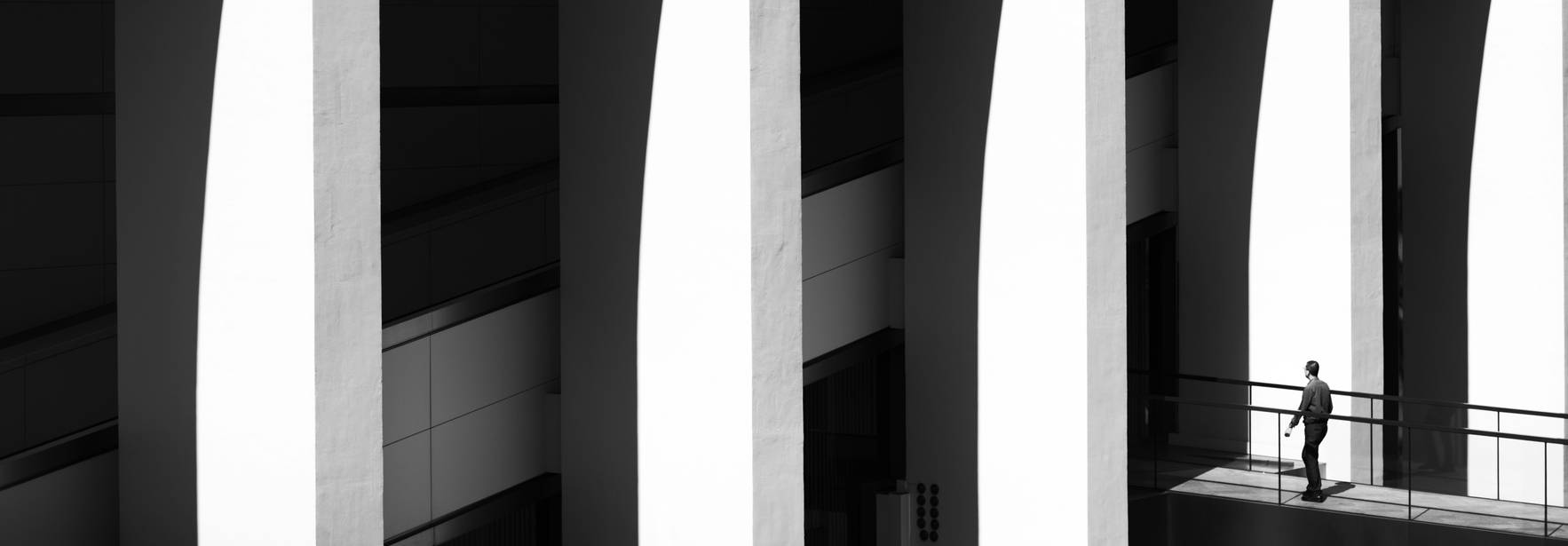Una persona camina bajo arcos en un entorno arquitectónico en blanco y negro.