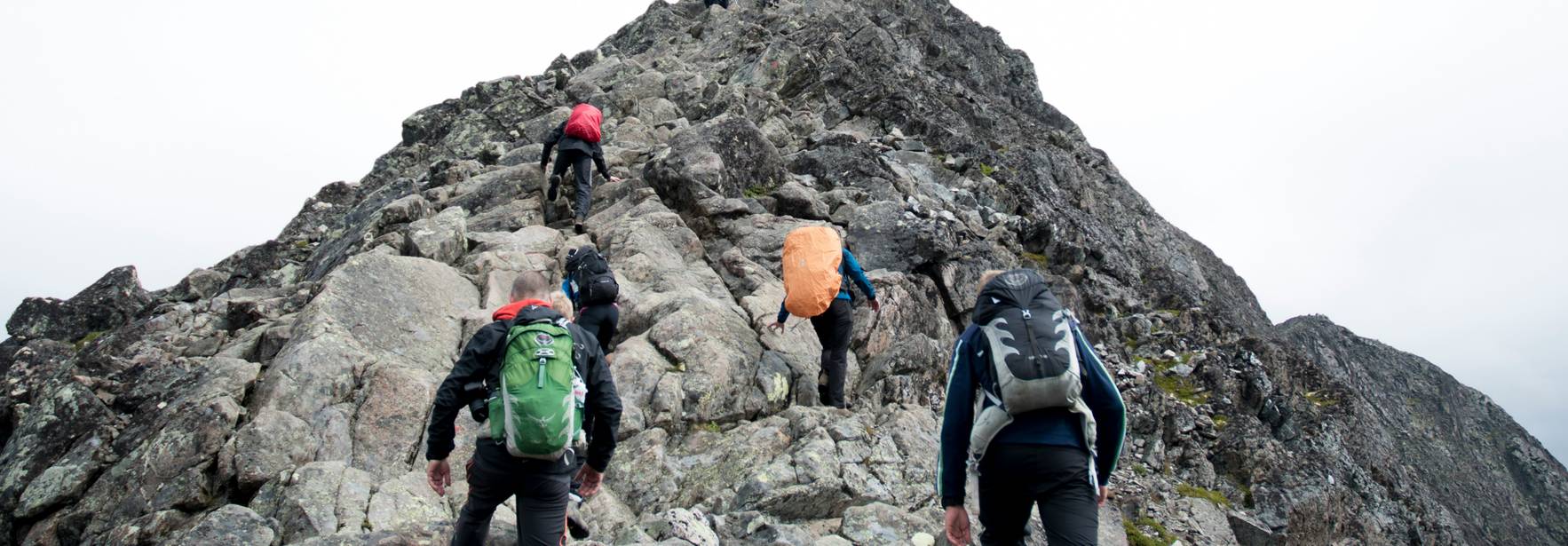 Grupo de personas ascendiendo una empinada ladera rocosa hacia una cima montañosa.