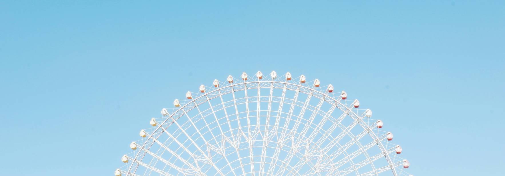 La imagen muestra una noria blanca contra un cielo azul claro.
