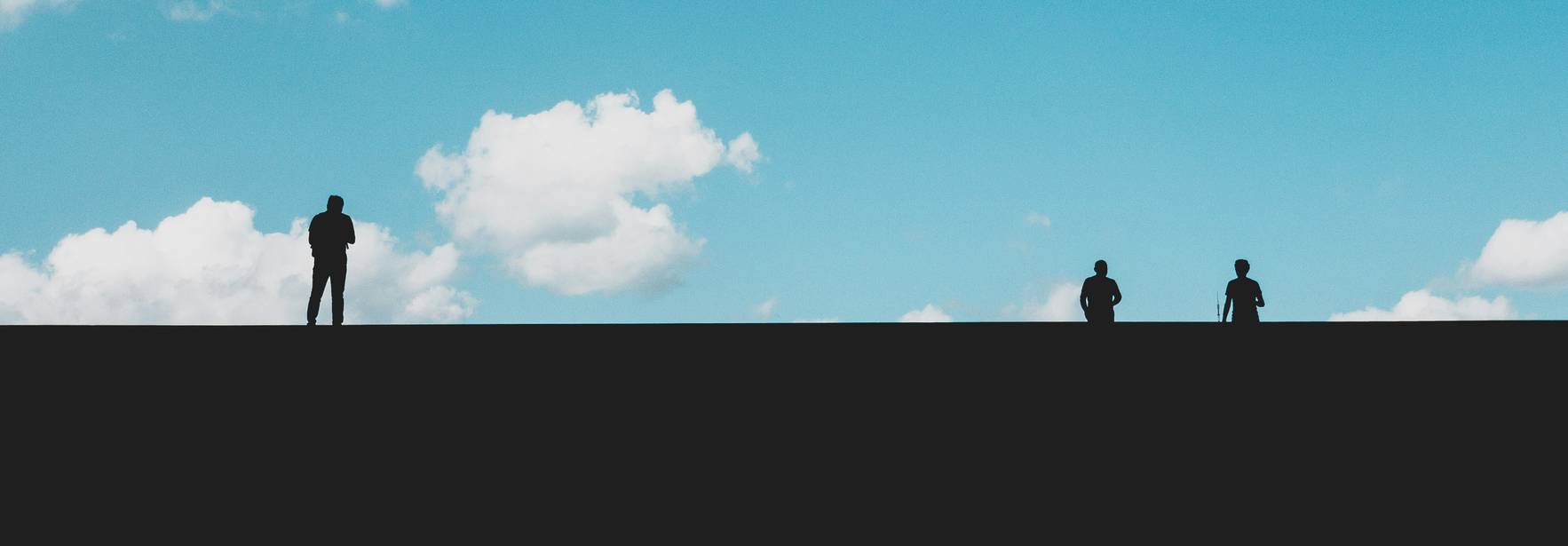 Un grupo de siluetas de personas se observa contra un fondo de cielo azul con nubes esponjosas.