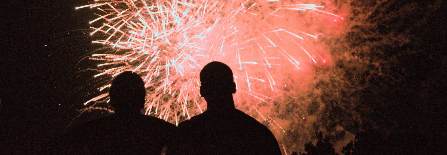 Dos personas observan un espectáculo de fuegos artificiales iluminando el cielo nocturno.