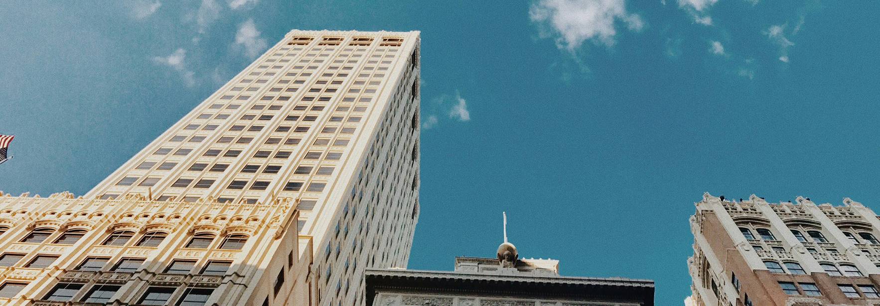 Una vista desde el suelo hacia los rascacielos bajo un cielo azul con algunas nubes.