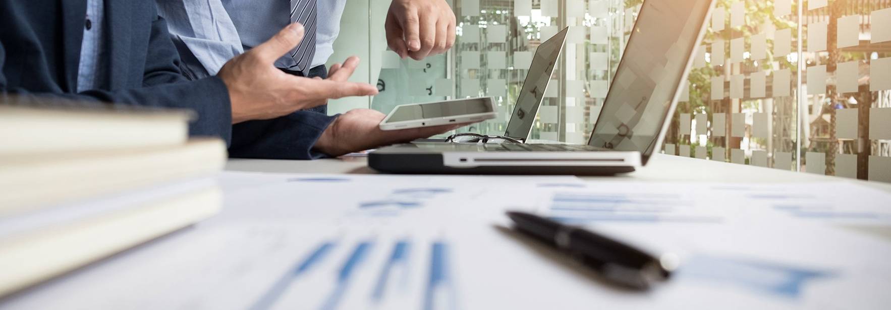 Dos personas discuten sobre un proyecto mientras consultan dispositivos electrónicos en un entorno de oficina.