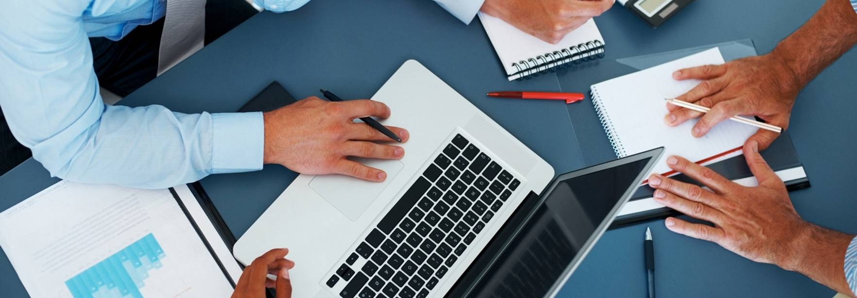 Un grupo de personas trabaja en equipo alrededor de una mesa con una computadora portátil y documentos.