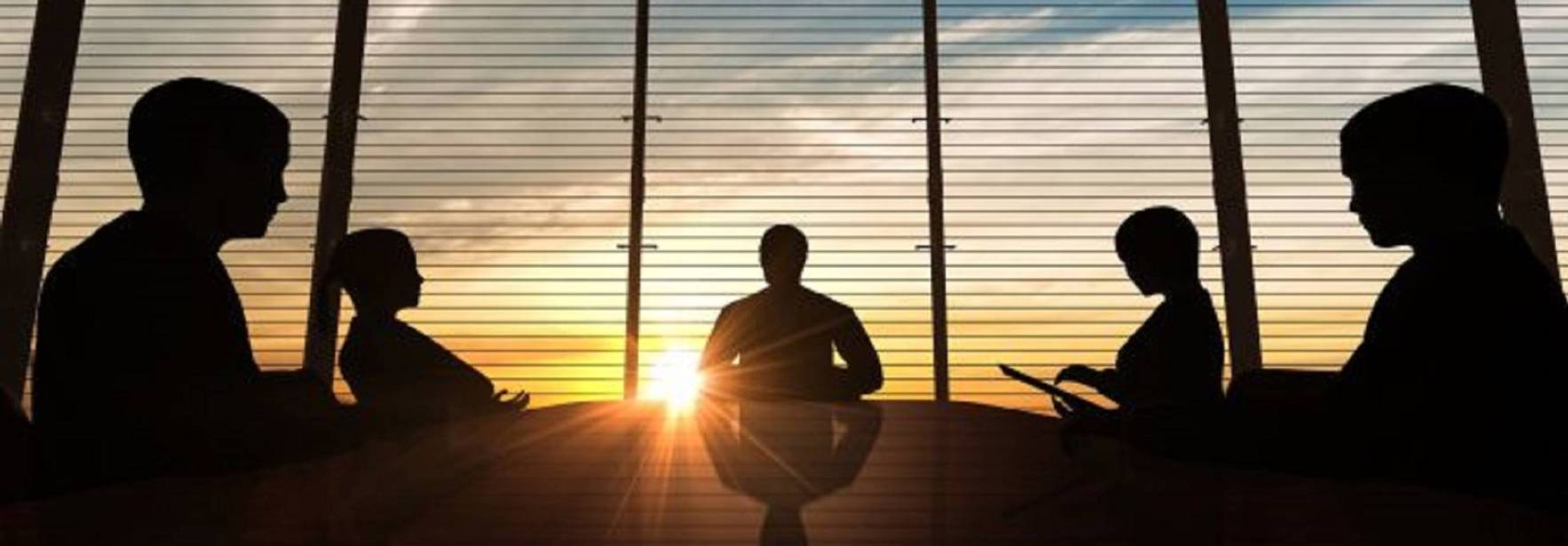 Siluetas de cinco personas en una reunión con un fondo de ventanas que muestran un atardecer.