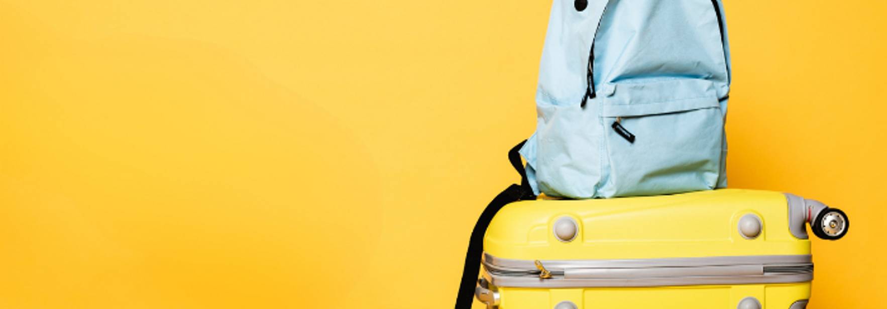 Una mochila azul sobre dos maletas amarillas en un fondo amarillo.