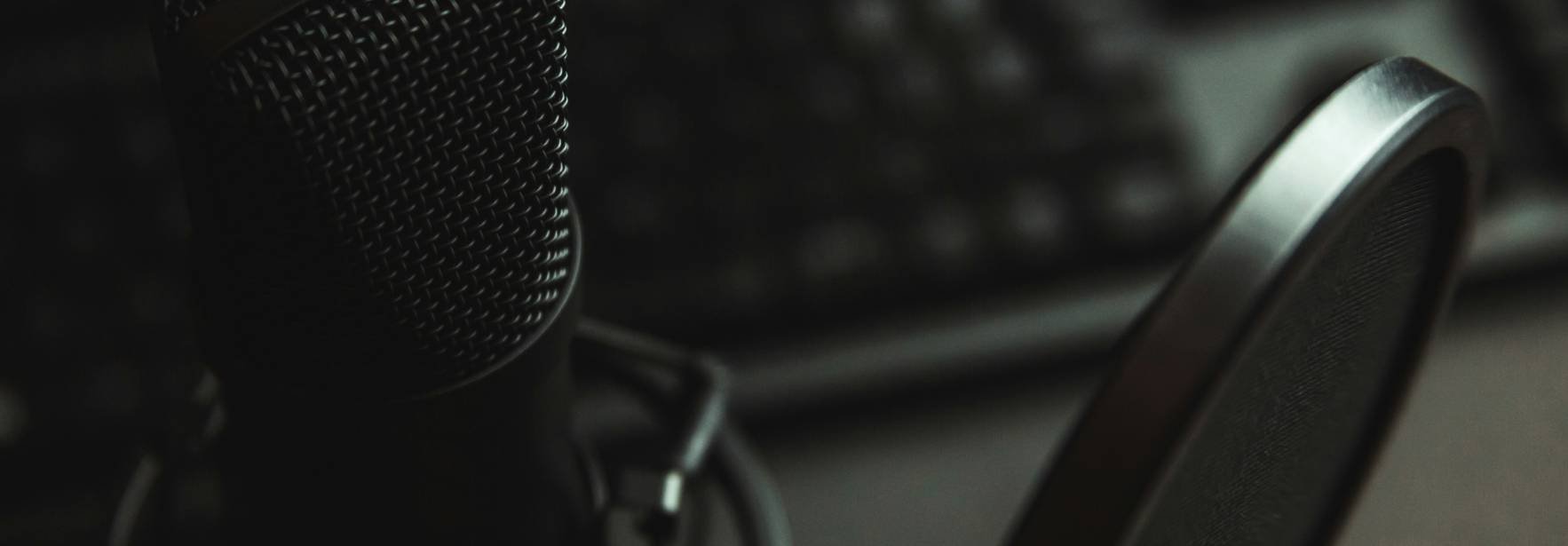 Un micrófono de estudio se encuentra en primer plano, con un teclado difuminado al fondo.