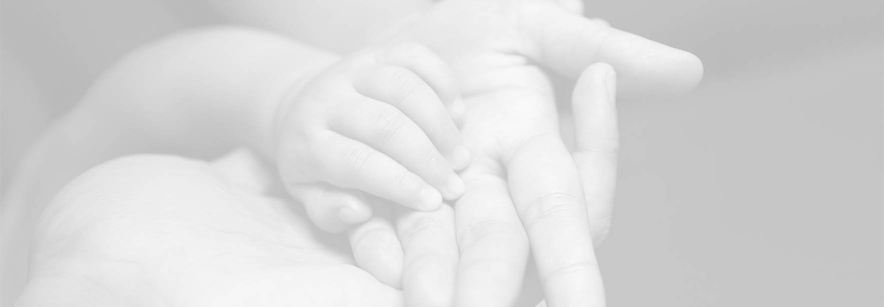 Una mano de un adulto sostiene delicadamente la mano de un bebé.