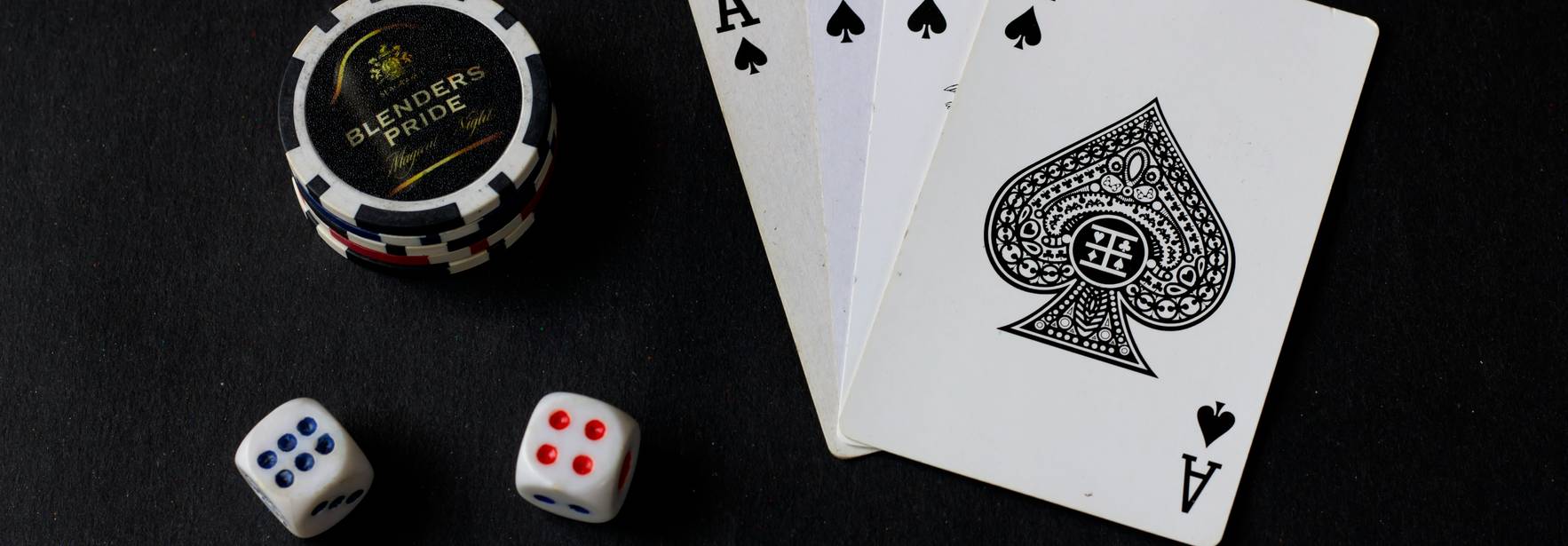 Una composición de cartas de póker, un ficho y dados sobre un fondo oscuro.