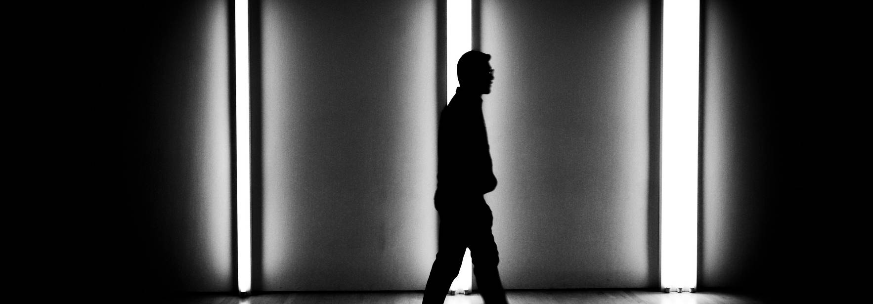 Un hombre camina en silencio entre luces blancas en un fondo oscuro.