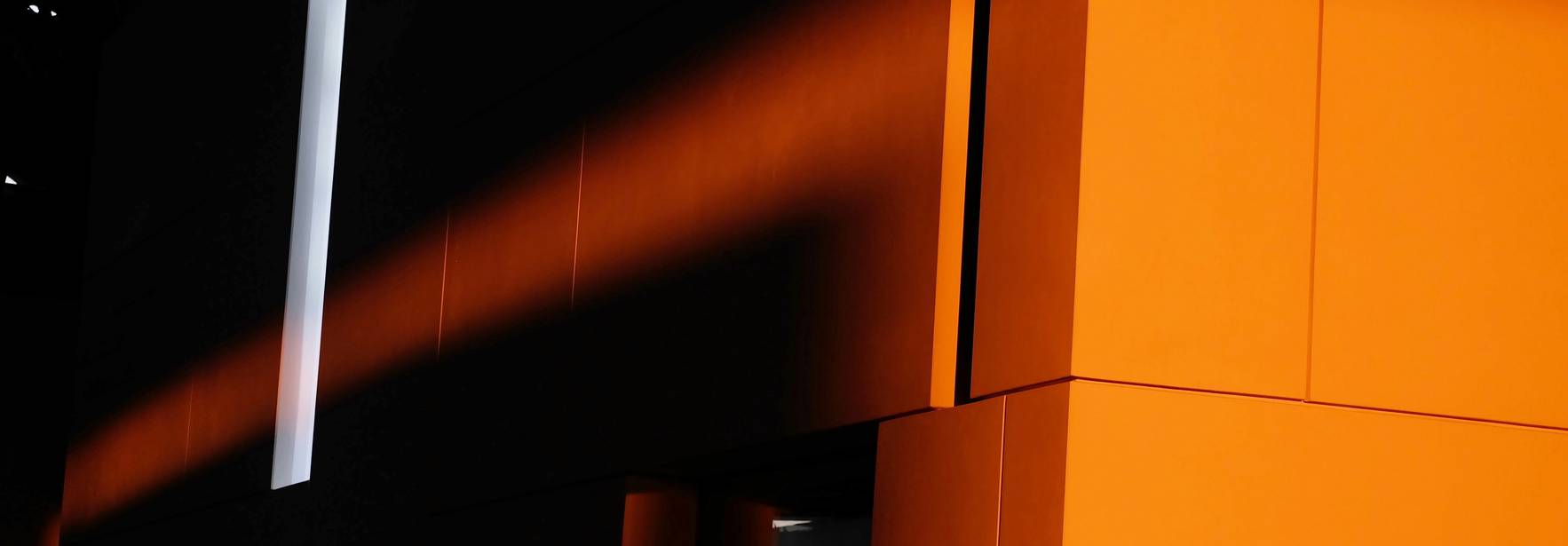 Un juego de luces y sombras sobre una pared naranja con un panel blanco.