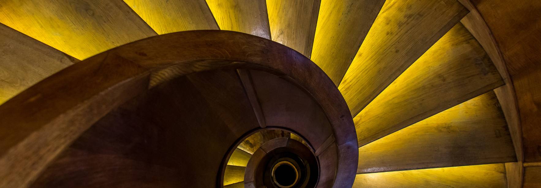 Una escalera de caracol iluminada con luces amarillas que resalta su diseño en espiral.
