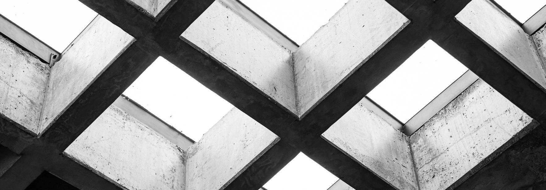 Una vista desde abajo de un techo de concreto con claros rectangulares que dejan pasar la luz.