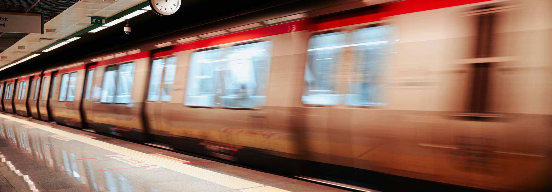 Un tren de metro pasa rápidamente por la estación, mientras un reloj muestra la hora en la pared.