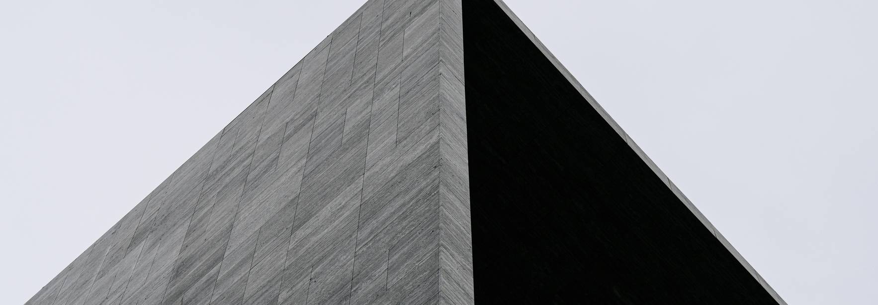 Una estructura arquitectónica con un diseño angular y materiales oscuros que se eleva contra un cielo nublado.