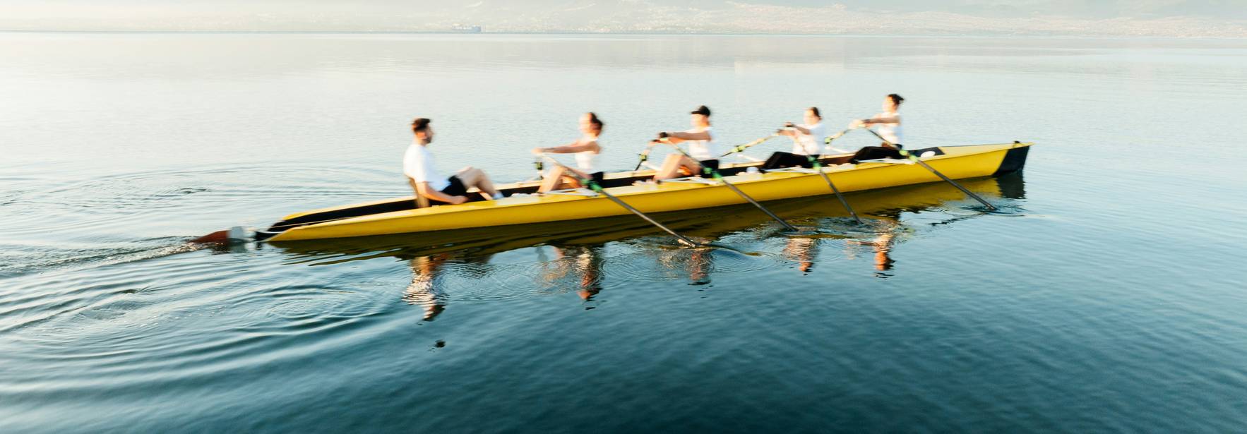 Un grupo de remeros en un bote amarillo navega por un lago sereno.