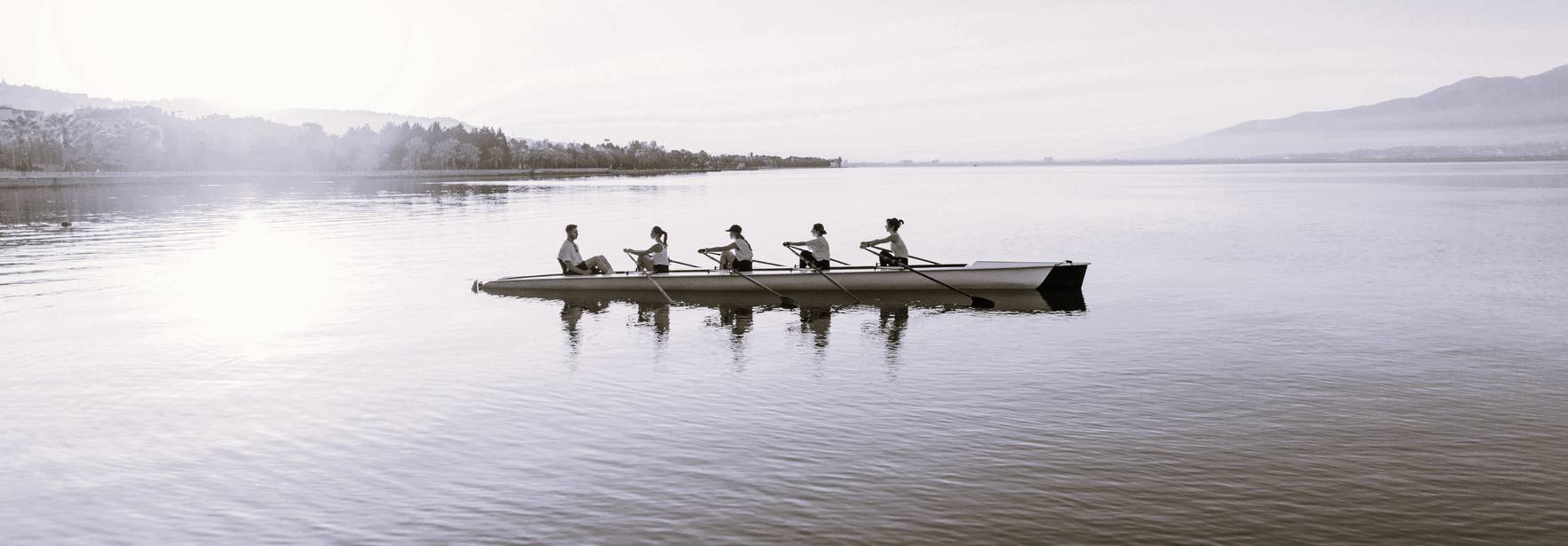 Un grupo de remeros entrenando en un bote a lo largo de un tranquilo lago al amanecer.