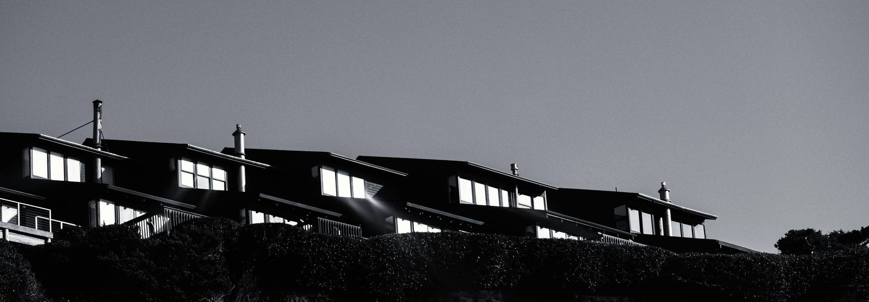 Una fila de casas oscuras se alza sobre un acantilado, iluminadas por la luz del sol.