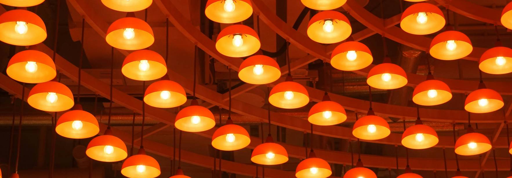 La imagen muestra una serie de lámparas colgantes de color naranja iluminadas.
