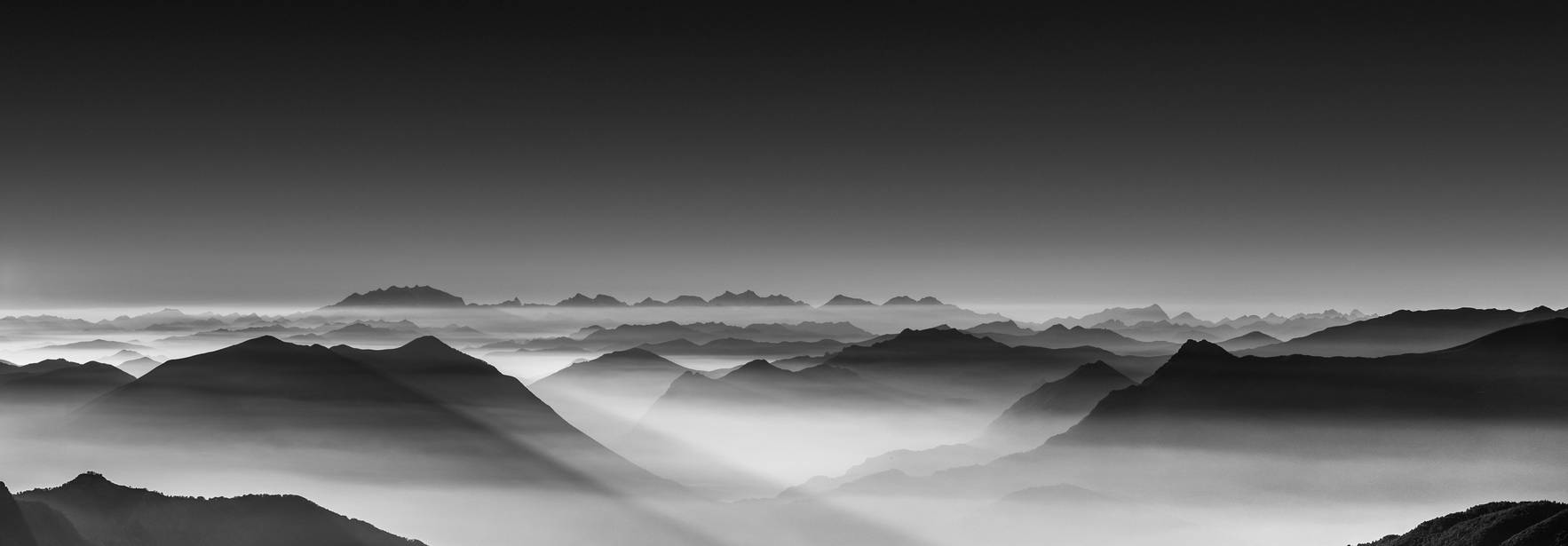 Una vista panorámica en blanco y negro de montañas cubiertas de niebla y neblina.