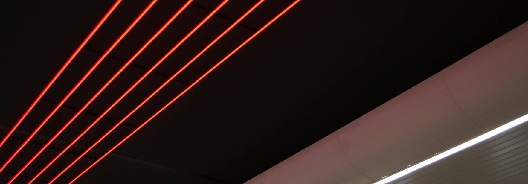 La imagen muestra un techo con líneas de luces rojas sobre un fondo oscuro y una franja blanca en la parte inferior.
