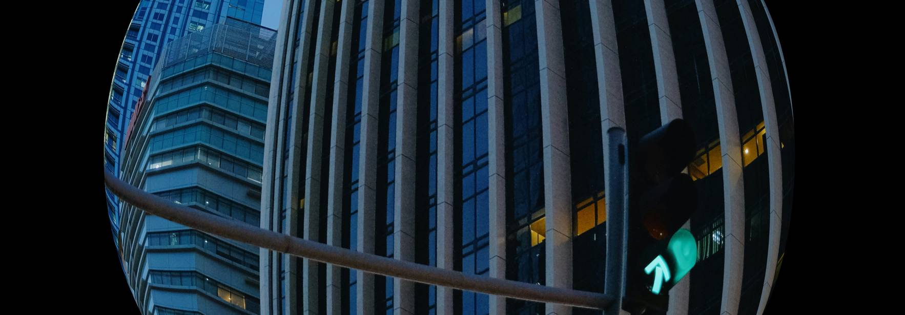 La imagen muestra un edificio con fachadas de vidrio reflejando el cielo nocturno y un semáforo con luz verde.
