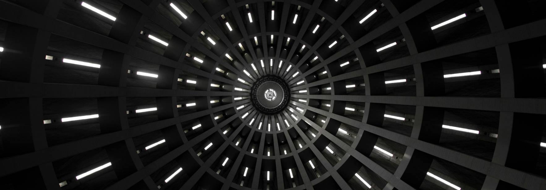 Una vista desde abajo de una estructura circular con luces que emanan de las paredes en un patrón radial.