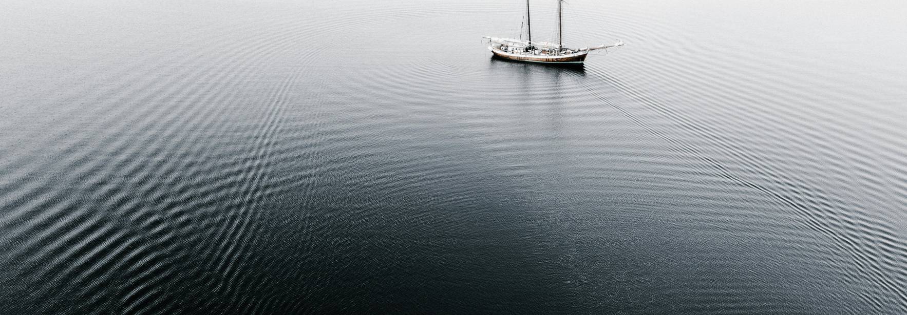 Un velero solitario navega en aguas tranquilas y oscuras bajo un cielo brumoso.