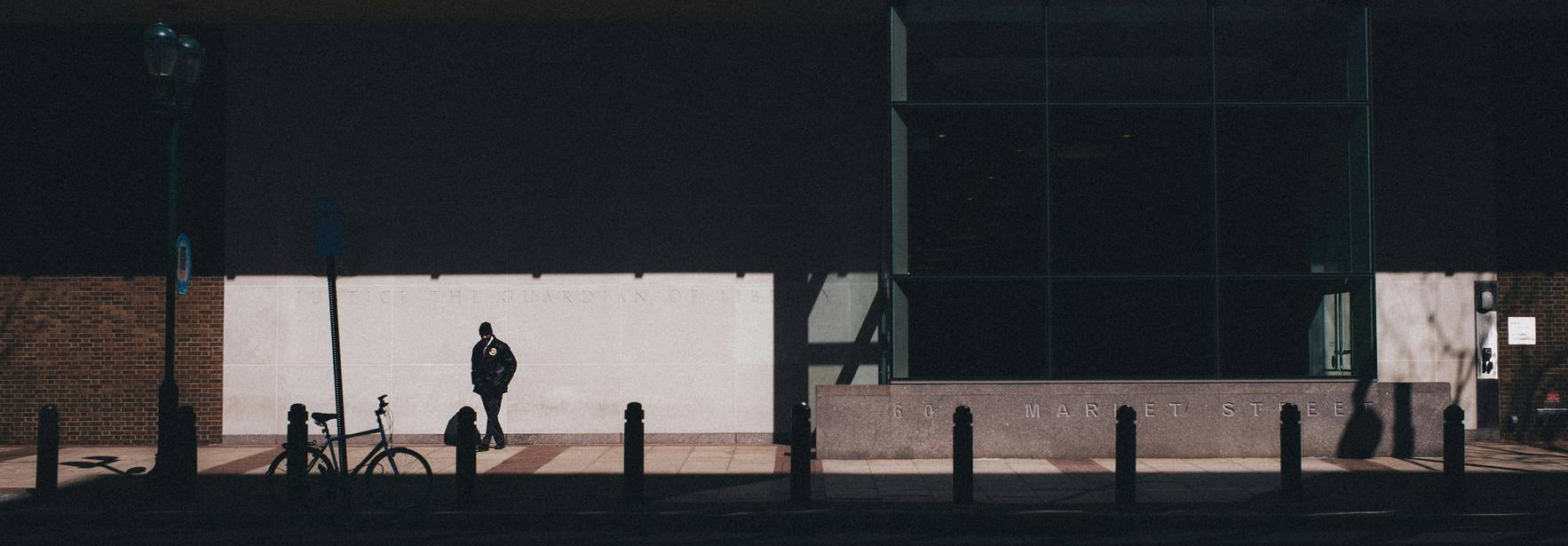 Una persona está de pie en la sombra frente a un edificio moderno.