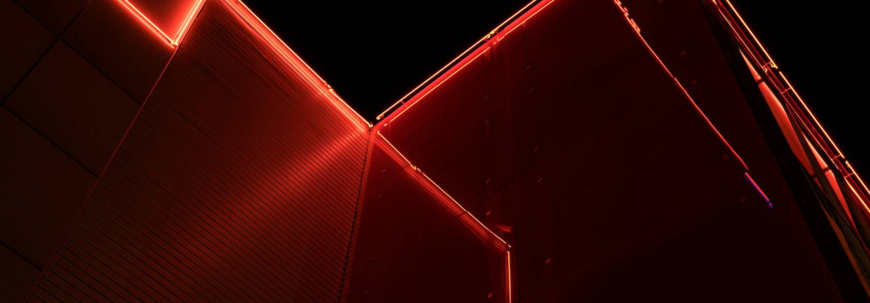 La imagen muestra una esquina de un edificio iluminado con luces rojas en la noche.