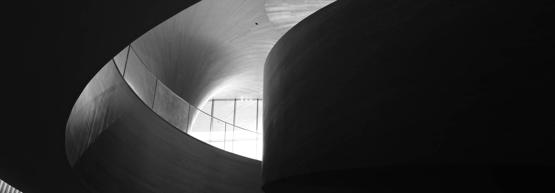 Una persona se encuentra en una estructura arquitectónica con curvas en un ambiente en blanco y negro.